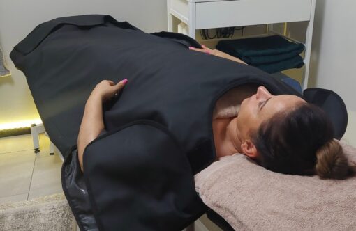 Gentle woman receiving SLIMM body contouring treatment in clinic, lying on treatment table with eyes closed, relaxing during fat reduction session, professional spa environment, non-invasive slimming therapy.